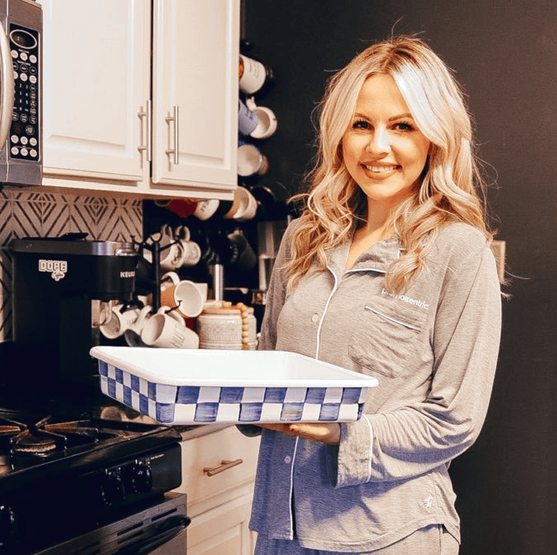 A smiling Woman holding a tray in a kitchen.
